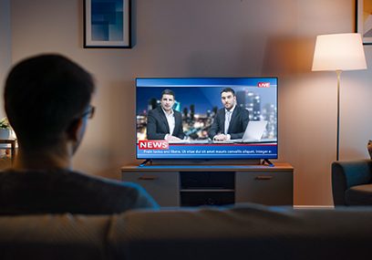 Young Man in Glasses is Sitting on a Sofa and Watching TV with L